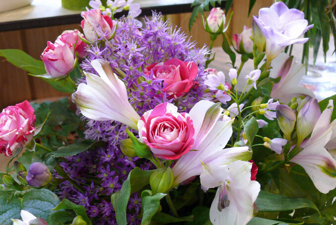 Ein farbenfroher Strauß mit rosafarbenen Rosen, weißen Lilien und kleinen lilafarbenen Blütenbüscheln, mit grünen Blättern im Hintergrund - perfekt für Geschenkideen oder um Floristik frisch geliefert zu bekommen mit unserem Lieferservice.